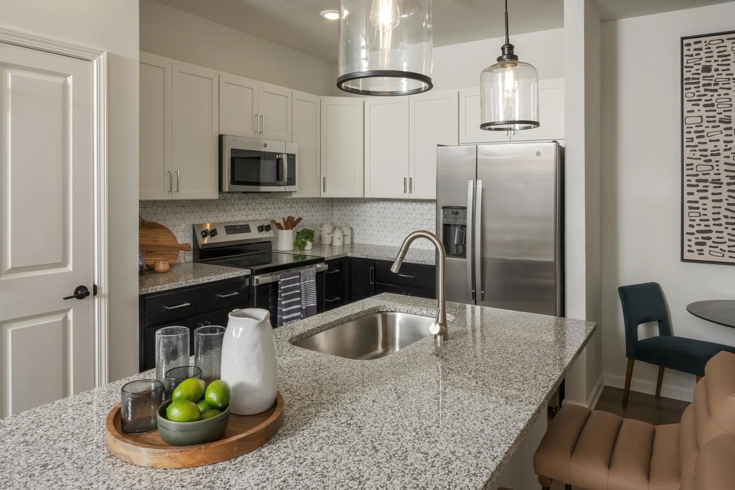 Evolve at the Pines modern kitchen with granite island, stainless steel appliances, and pendant lights over the countertop.