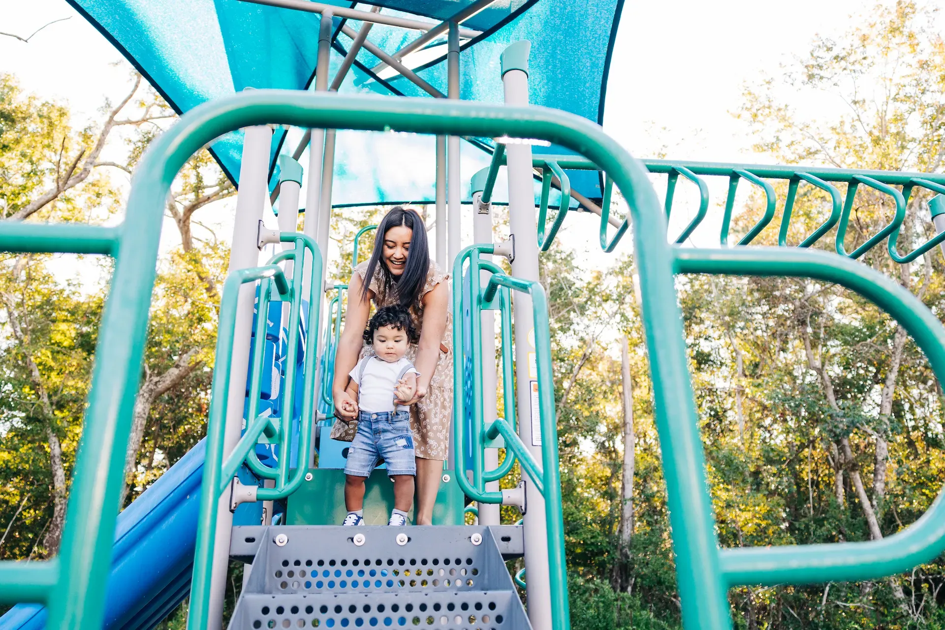 Evolve at the Pines A woman and a child joyfully sliding down a playground slide, enjoying a sunny day together.