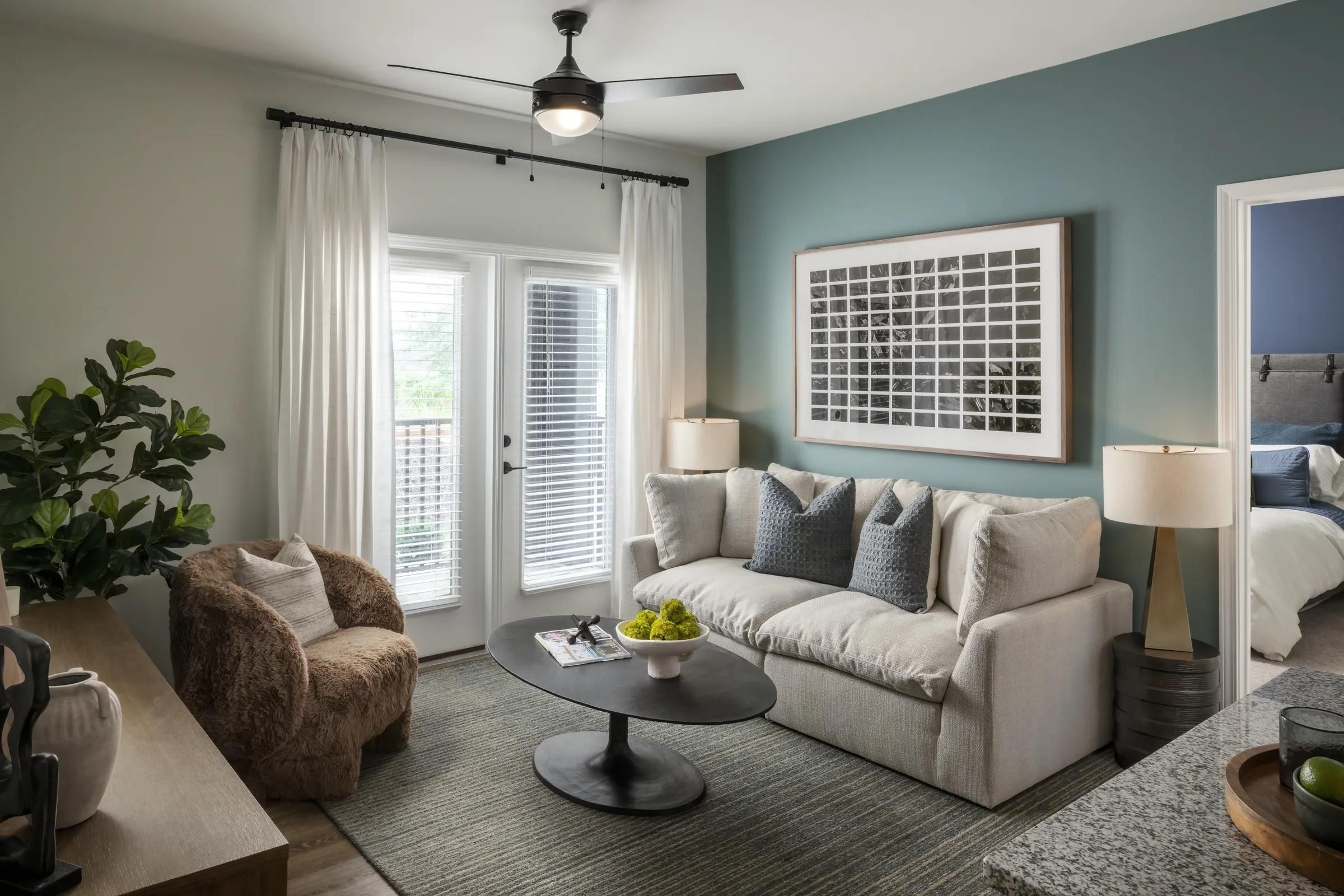 Evolve at the Pines modern living room with a white sofa, armchair, round coffee table, and French doors with sheer curtains.