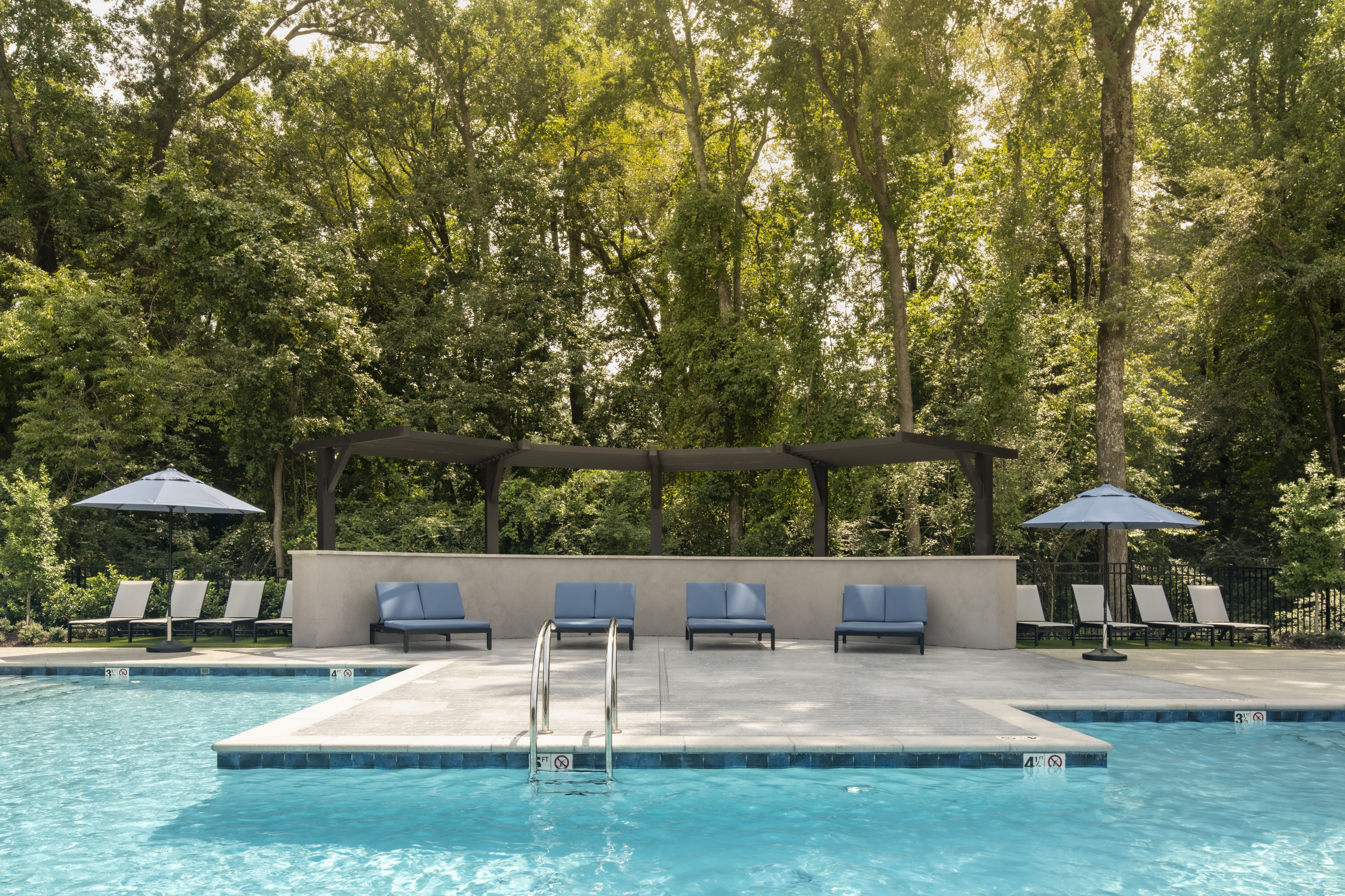 Modern apartment complex with a large outdoor swimming pool, lounge chairs, and surrounding buildings.